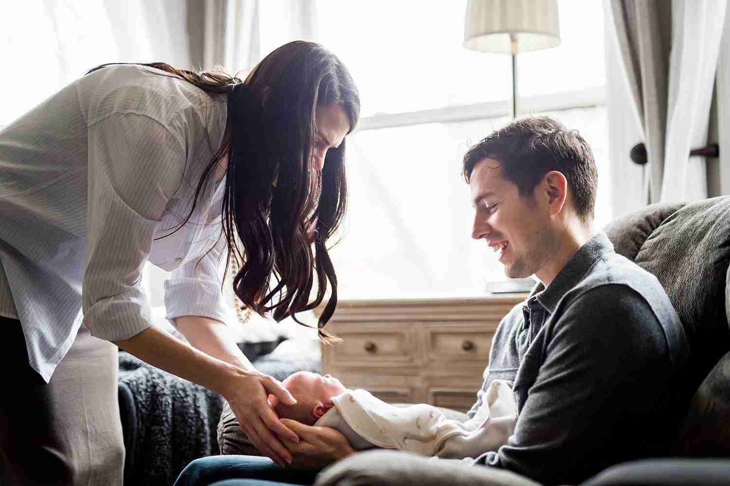 Photo of dad holding baby while mom leans over and cradles baby's head in her hands.