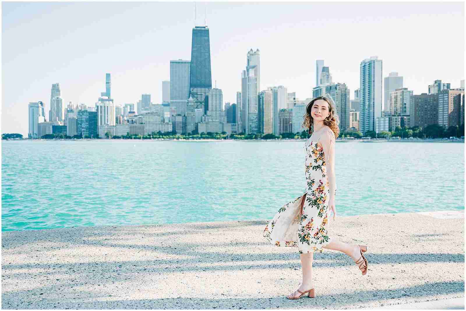 Booking Senior Photos - When to Book Your Senior Photography Session - girl wearing white floral dress walking at North Avenue Beach - award-winning Chicago senior photographer Shalimar B. Photography.