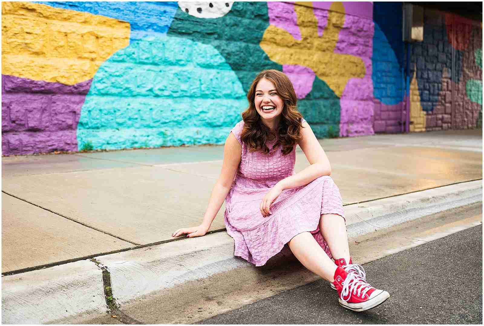 Preparing for your senior photos – 3 ways I help you prepare for your senior photos (senior girl wearing pink dress and red Converse sneakers sitting & smiling in front of colorful mural in Chicago) with award-winning Chicago senior photographer Shalimar B. Photography.