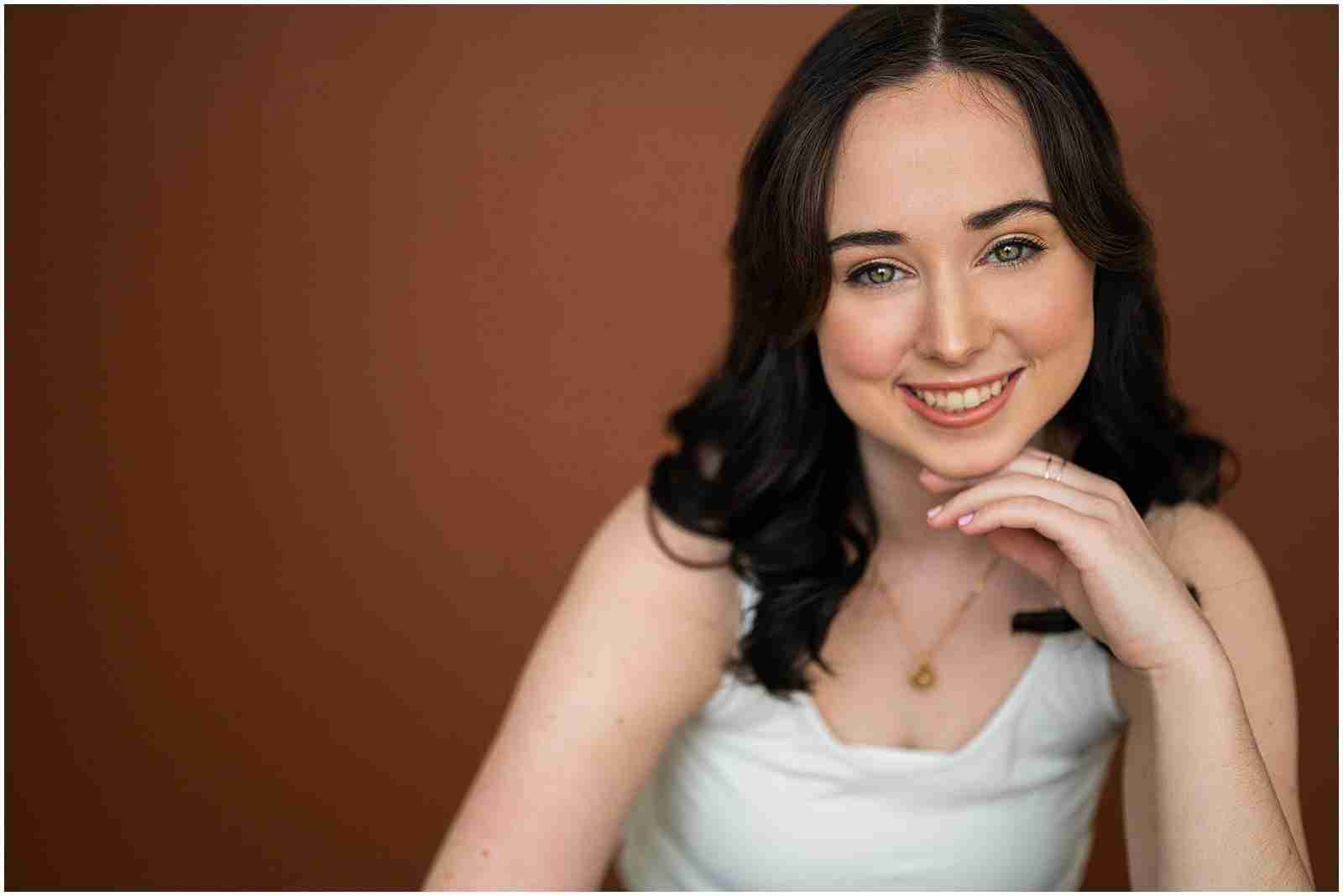 What you can expect at every senior session with SBP - senior girl wearing white tank top and jeans on brown backdrop at studio - award-winning Chicago senior photographer Shalimar B. Photography.