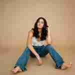 What to Ask Your Senior Photographer Before Booking – senior girl wearing white crochet top sitting on tan studio backdrop – award-winning Chicago senior photographer Shalimar B. Photography.